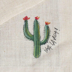 Cactus con fiori rossi alle estremità, disegnato su una tovaglia in canapa, a lato la scritta "viva la vida"